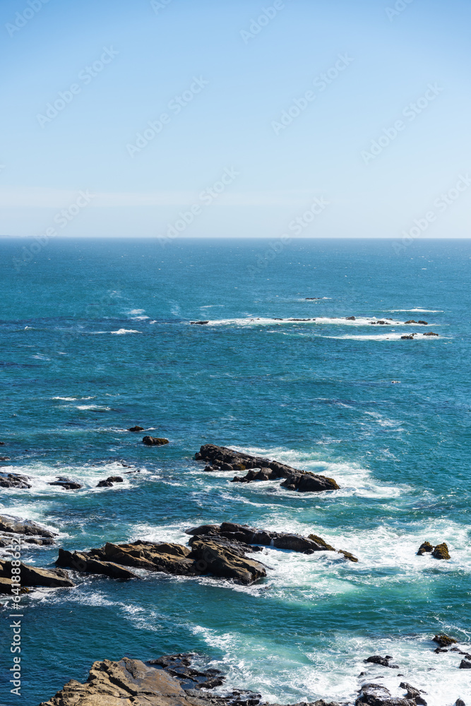 Waves crashing on rocks in the Pacific Ocean on blue sky day