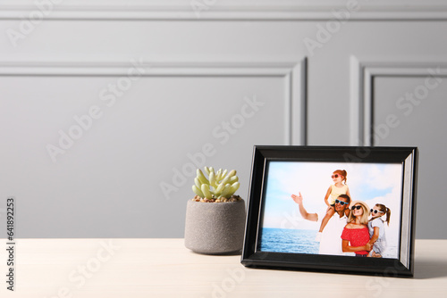 Frame with family photo and houseplant on white table near grey wall  space for text