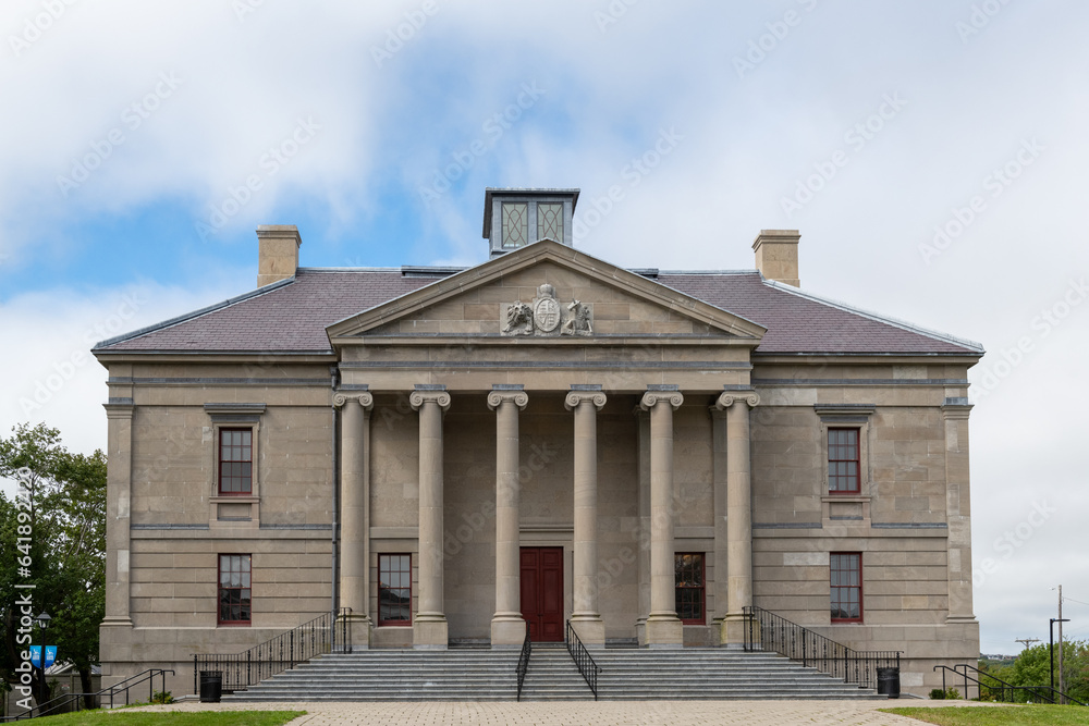 A wide brick entrance to a large courthouse, justice, or government style building. There's a tall red door, grey marble steps, black handrails, tall windows, round pillars, and a beige exterior wall.