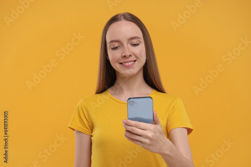 Happy young woman using smartphone on yellow background