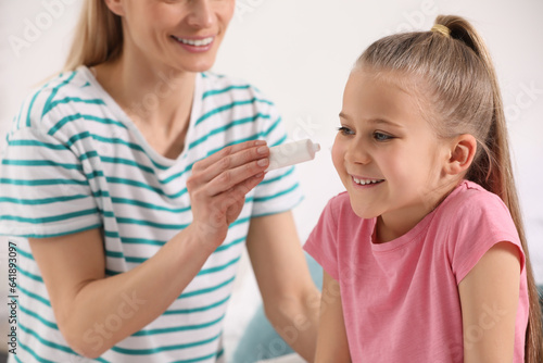 Mother applying ointment onto her daughter's cheek on white background