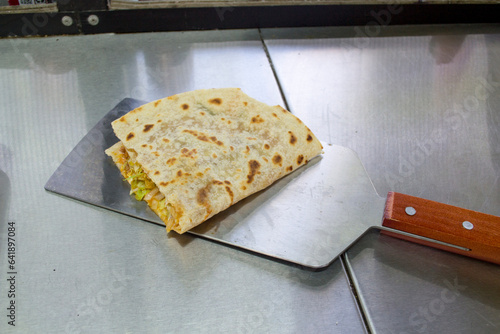 Tortilla típica de harina con guisado, taco pirata partido a la mitad con espátula de aluminio. comida callejera mexicana. photo