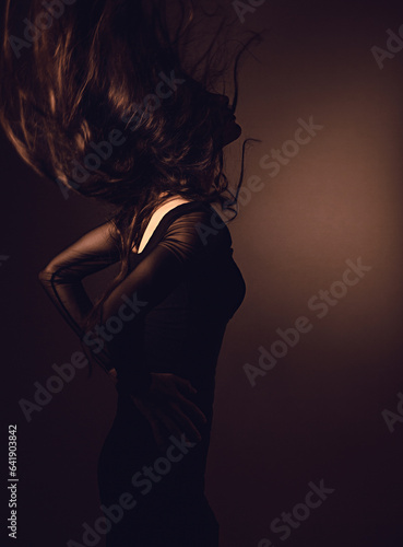 Silhouette of beautiful girl with sporty slim figure in black dress moving with hair above the head on dark shadow art background. Closeup