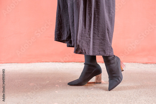 Female legs in black autumn boots against background of concrete and a pink wall.