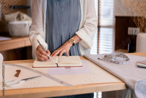 Asian tailor women creative and designing new fashion collection while drawing sketch in notebook