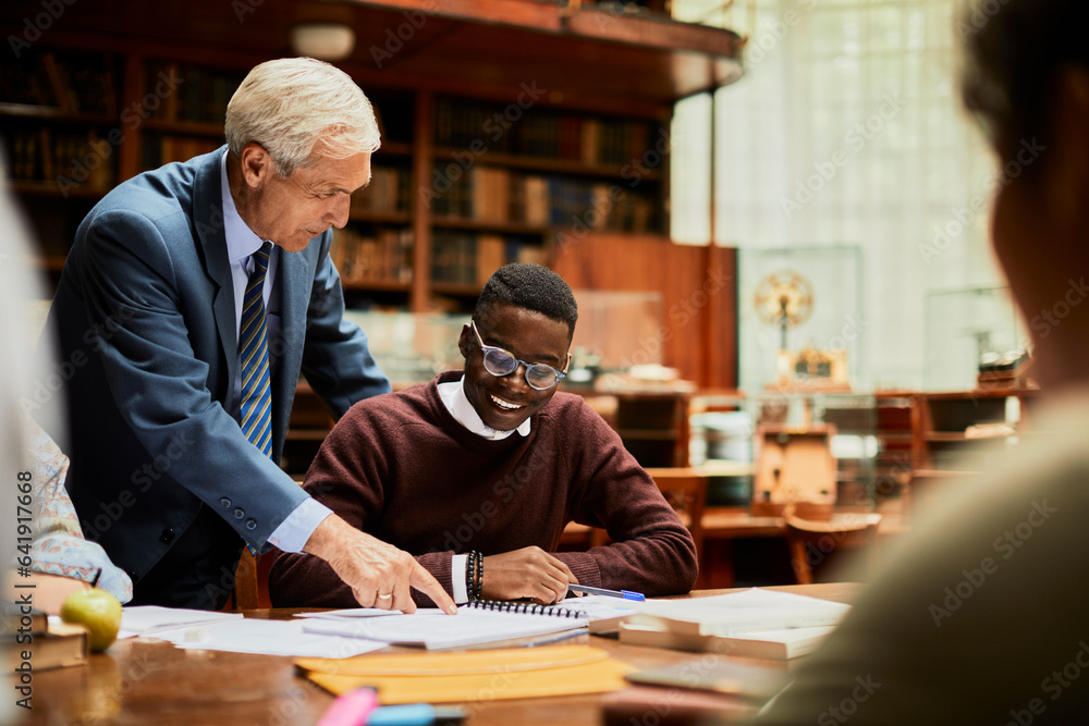 Young and diverse group of students studying in a university library with the help of their professor Young and diverse group of students studying in a university library with the help of their professor