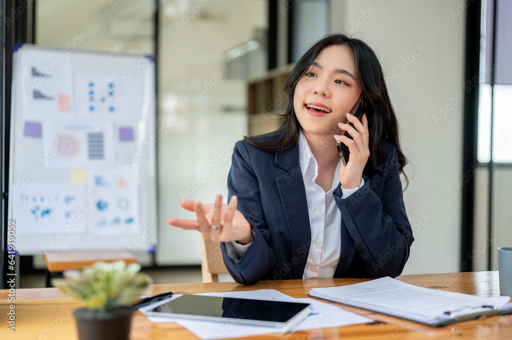 A professional Asian businesswoman is talking on the phone with a business client at her desk. A professional Asian businesswoman is talking on the phone with a business client at her desk.