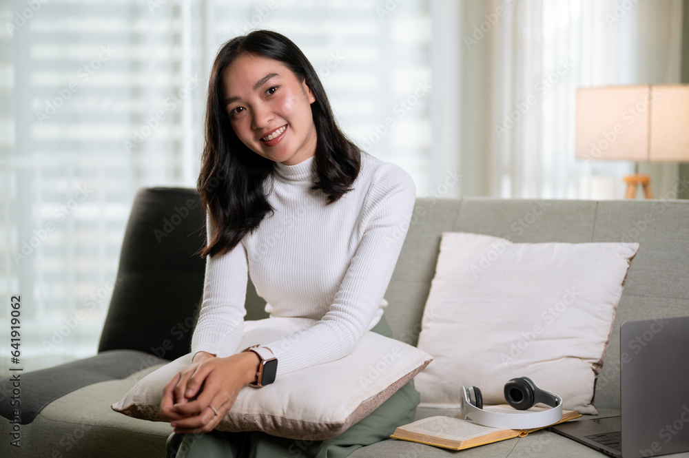 A beautiful Asian woman in comfy clothes sits on a comfortable sofa in the living room A beautiful Asian woman in comfy clothes sits on a comfortable sofa in the living room