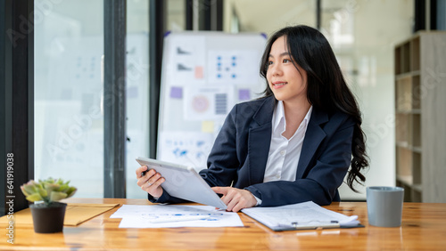 A charming Asian businesswoman sits at her desk, daydreaming about her career success.