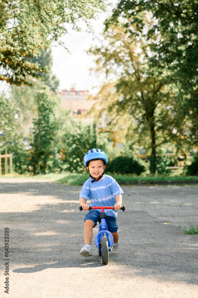 Happy child riding balance bike. Male toddler kid in helmet learning to ride on run bicycle Happy child riding balance bike. Male toddler kid in helmet learning to ride on run bicycle