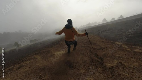 Following POV: Woman runs, glissades down foggy ash slope of volcano photo