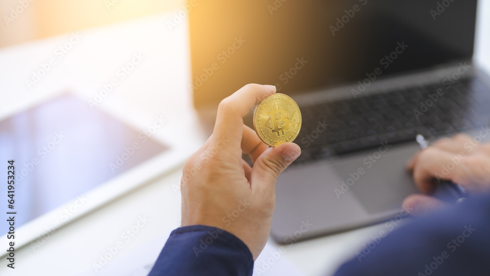 Businessman hand holds gold Bitcoin logo symbol Crypto using computer laptop for trading, money investment on Bitcoin Cryptocurrency. Trading Bitcoin Crypto on mobile app or online internet platform.