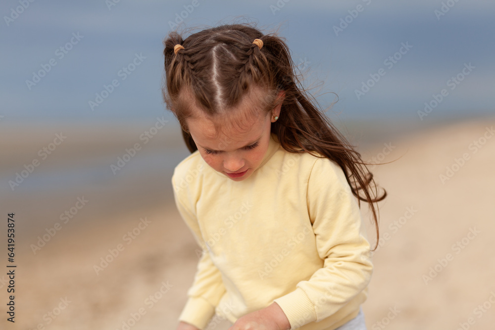 A little girl in a yellow sweater runs along the sandy beach. Blurred sea background. Happy vacation days A little girl in a yellow sweater runs along the sandy beach. Blurred sea background. Happy vacation days
