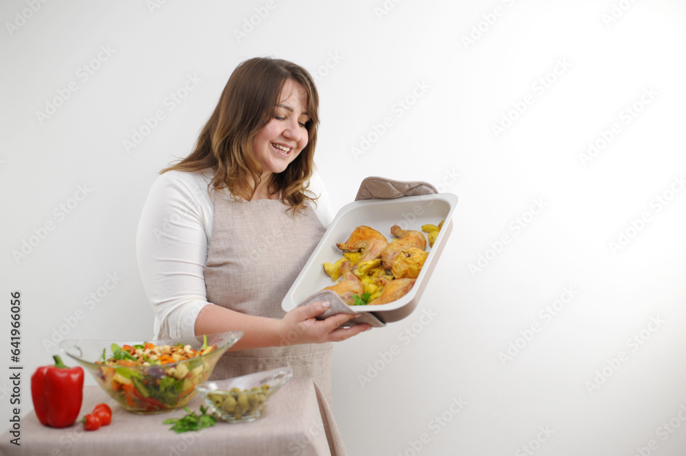 happy satisfied beautiful plump woman with a baking sheet in her hands delicious food chicken legs salad freshly prepared dinner for the family on a white background cook tasty laugh sincere facial