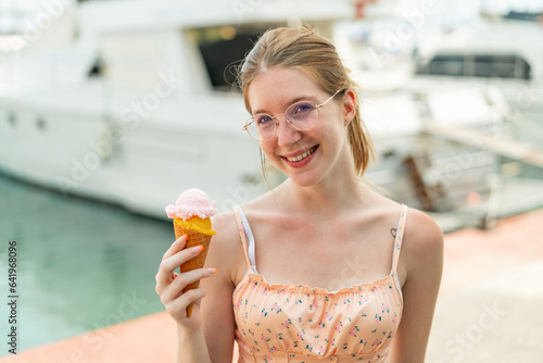 French girl with glasses holding a cornet ice cream at outdoors smiling a lot