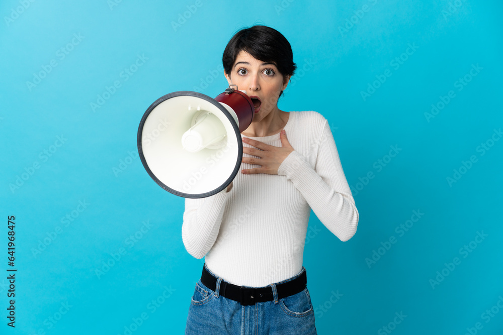 Woman with short hair isolated on blue background shouting through a megaphone with surprised expression Woman with short hair isolated on blue background shouting through a megaphone with surprised expression
