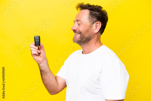 Middle age caucasian man holding car keys isolated on yellow background with happy expression © luismolinero