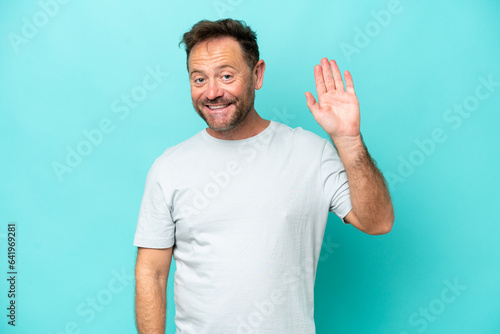 Middle age caucasian man isolated on blue background saluting with hand with happy expression