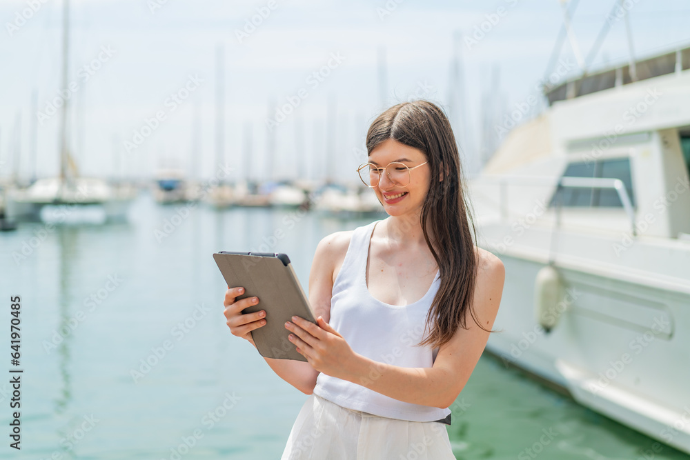 Young pretty Ukrainian woman holding a tablet at outdoors with happy expression