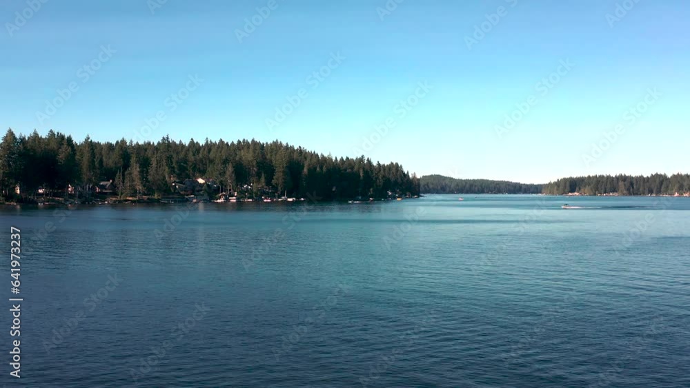 Aerial dolly push in above placid lake as speed boats rush below, homes on waters edge below dense pine tree forest Aerial dolly push in above placid lake as speed boats rush below, homes on waters edge below dense pine tree forest