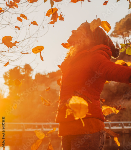 Winter is coming. Autumn sunset and happy woman throwing leaves in the air opening arms and smiling with happiness. Serene wellbeing people and natural healthy lifestyle. Outdoor leisure activity lady