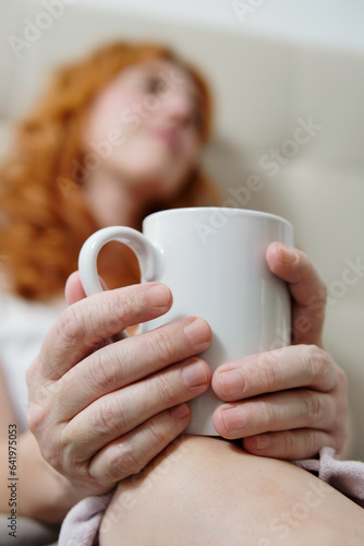 hands with cup in foreground with woman out of focus