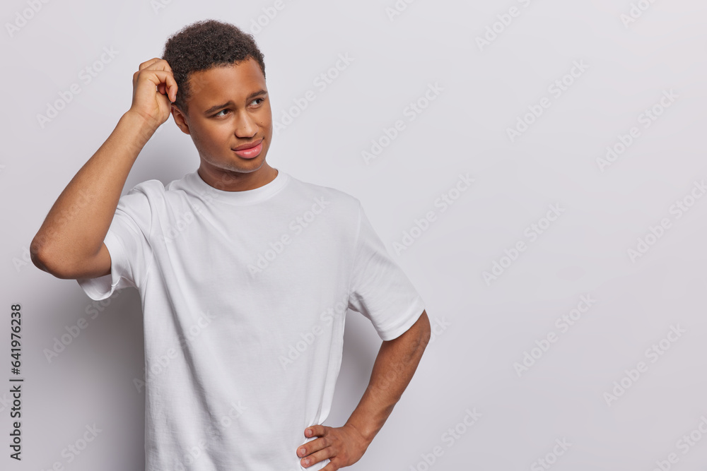 People emotions concept. Studio shot of young hesitant African american man standing on left isolated on white background making decision scraching head with blank space for your advertisement People emotions concept. Studio shot of young hesitant African american man standing on left isolated on white background making decision scraching head with blank space for your advertisement