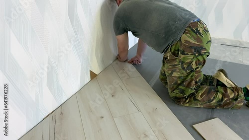 Laying a gray laminate board in the grooves. Repair of apartments. Man installing new laminate wood floor, home improvement, home remodeling project concept. High quality 4k footage