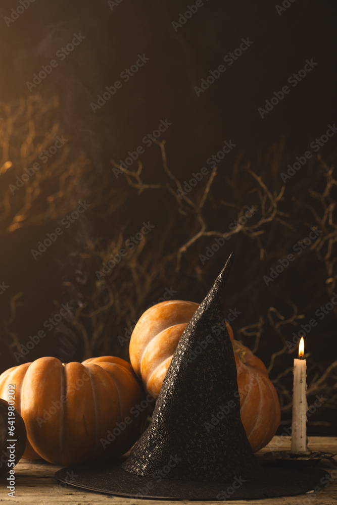 Fototapeta premium Vertical image of pumpkins and witch hat and burning candle with copy space on black background