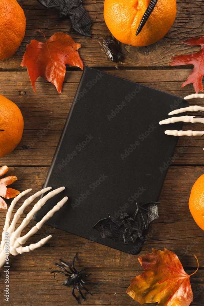 Fototapeta premium Vertical image of halloween decorations, skeleton hands on notebook, copy space on brown background