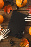 Vertical image of halloween decorations, skeleton hands on notebook, copy space on brown background