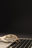 Vertical image of plastic skeleton hand on laptop keyboard with copy space on black background