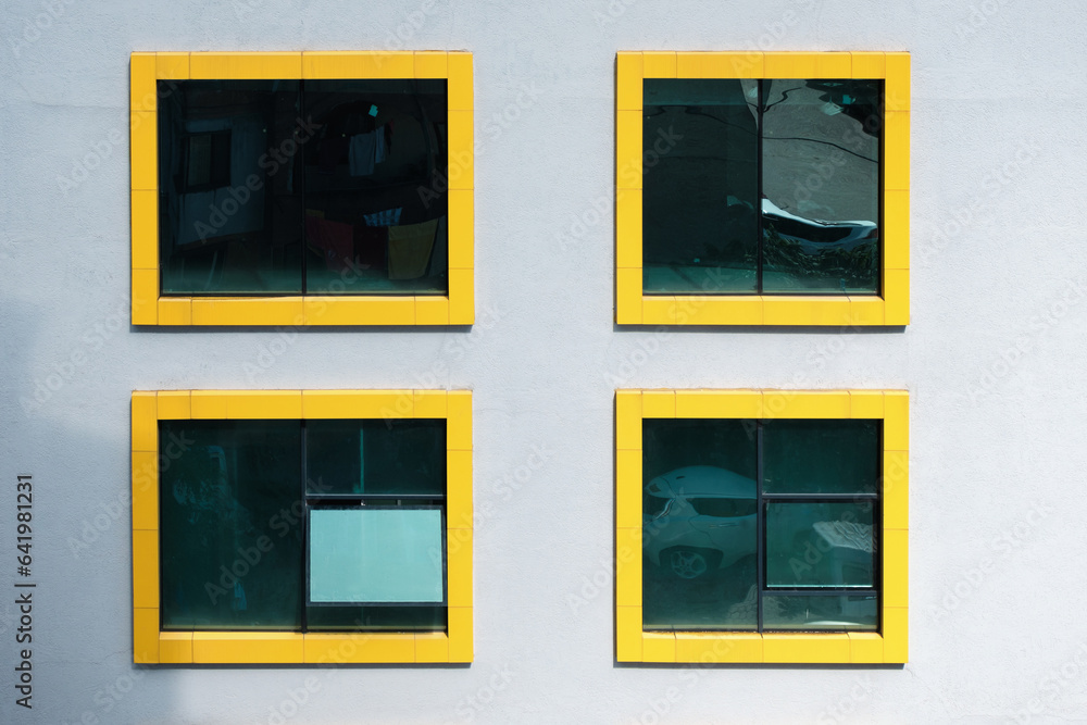 Four windows with yellow frames in a white color wall. Exterior of a building with yellow frame windows. Four windows with yellow frames in a white color wall. Exterior of a building with yellow frame windows.