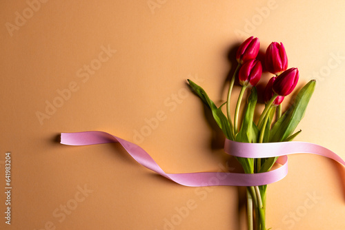 Vertical image of bunch of red tulips with pink ribbon and copy space on orange background