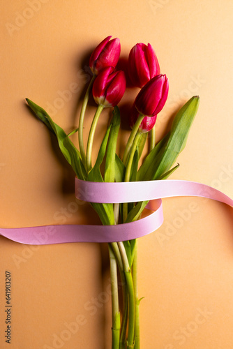 Vertical image of bunch of red tulips with pink ribbon and copy space on orange background