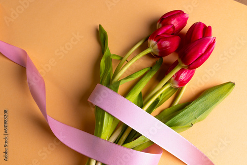 Bunch of red tulips with pink ribbon and copy space on orange background