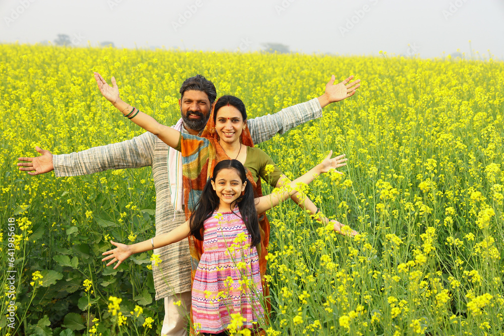 rural Indian family of a mother, father, and daughter standing in a mustard field and all of them are happy to see agricultural benefits of the field rural Indian family of a mother, father, and daughter standing in a mustard field and all of them are happy to see agricultural benefits of the field