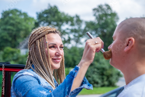 A woman with African braids applies powder to a man face with a powder brush. Copy space
