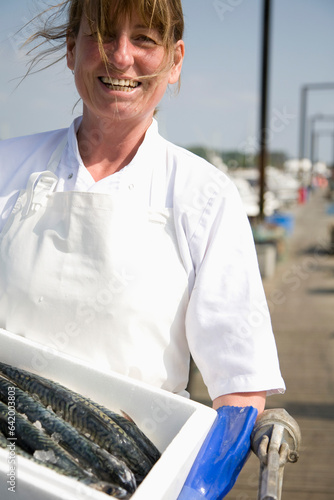 Portrait of smiling fishmonger holding a white container full of fish
