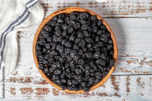 Natural dried blueberry grains in bowl on wooden background. Fruit snack for a health diet and alternative desert. Top view