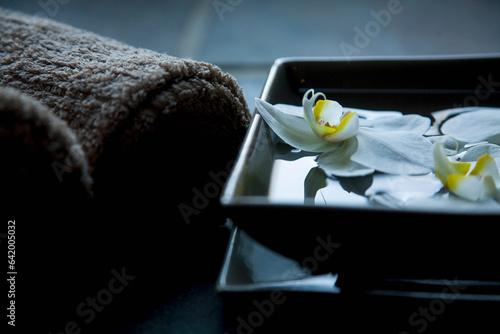 White flowers floating in square bowl with brown towels
 photo