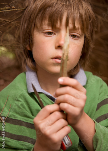 Close up of young boy sharpening a wooden stick in a campsite
 photo