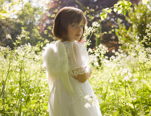 Portrait of young girl in a white fairy costume standing in a garden
 photo