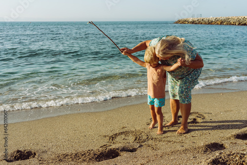 grandmother draws in the sand with her grandson on the beach near the sea photo