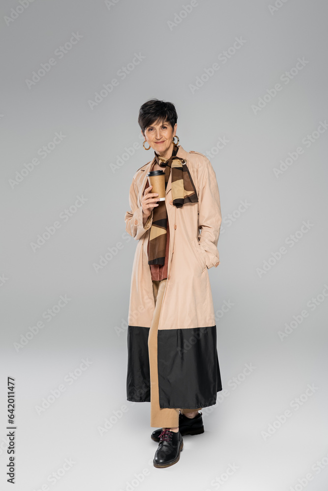 fashionable mature woman with takeaway drink on grey, autumn look, trench coat, scarf, full length fashionable mature woman with takeaway drink on grey, autumn look, trench coat, scarf, full length