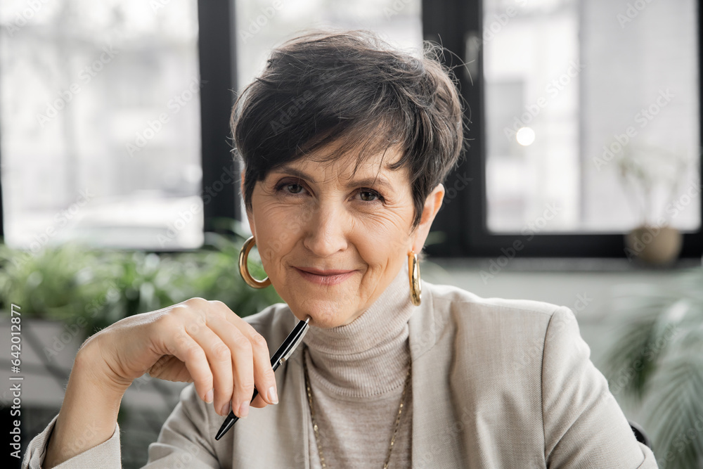 mature woman entrepreneur with pen looking at camera in office, experience, professional headshot mature woman entrepreneur with pen looking at camera in office, experience, professional headshot
