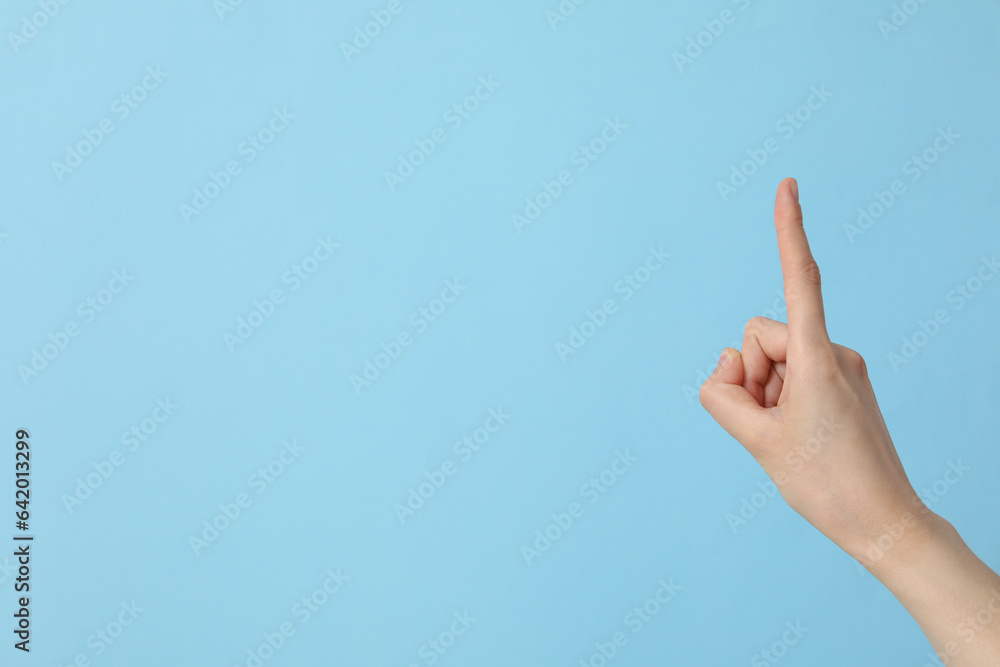 Female hand showing index finger on blue background, place for text Female hand showing index finger on blue background, place for text