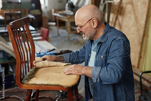 Side view portrait of senior man in furniture restoration workshop fixing old chair photo