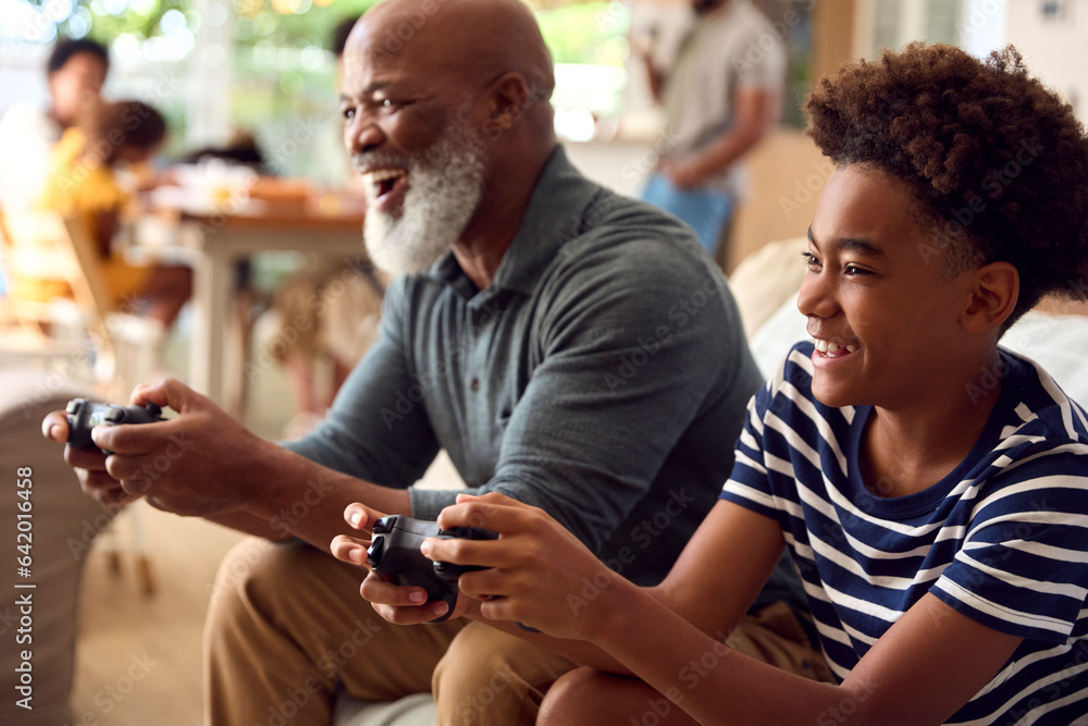 Fototapeta premium Grandfather And Grandson Sitting On Sofa At Home Playing Video Game Together