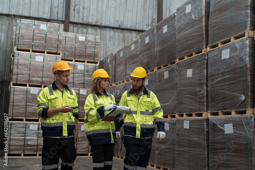 Male and female warehouse workers working and inspecting quality of plank of wood on shelves pallet at wooden warehouse storage. Group of warehouse workers discussing, checking products in warehouse